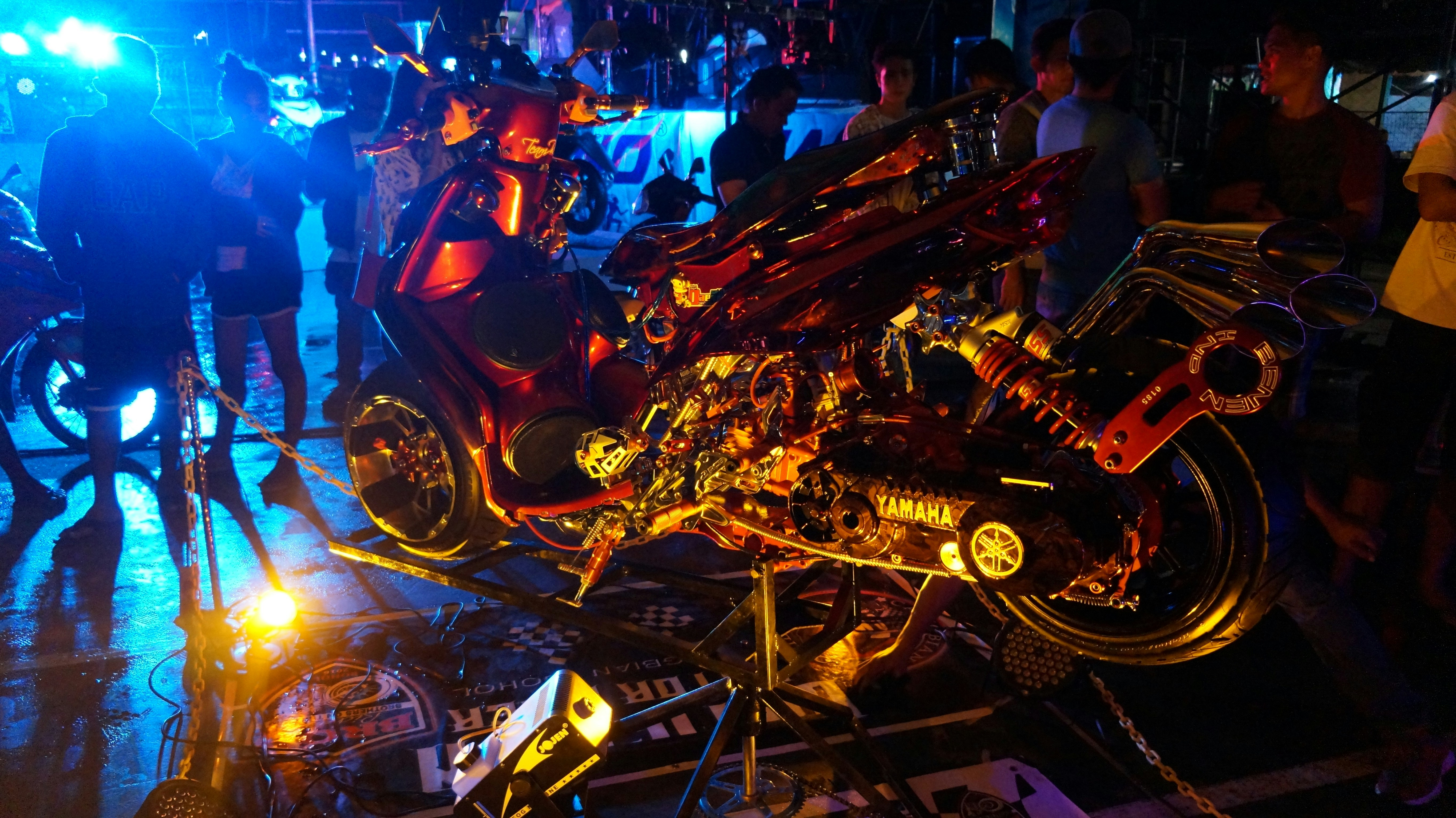 Custom motorcycle show with gleaming chrome and matte black bikes under dramatic spotlights, crowd gathering