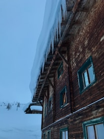 A rugged men’s winter coat hanging on a wooden rack with snow gently falling outside a cabin window.
