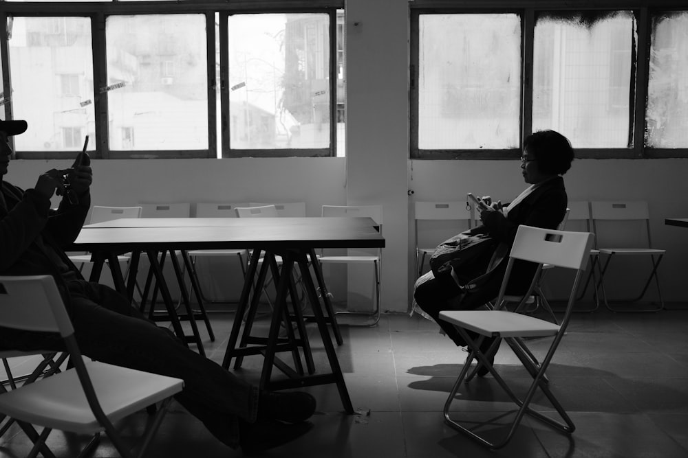 grayscale photo of two person sitting on chair inside the room