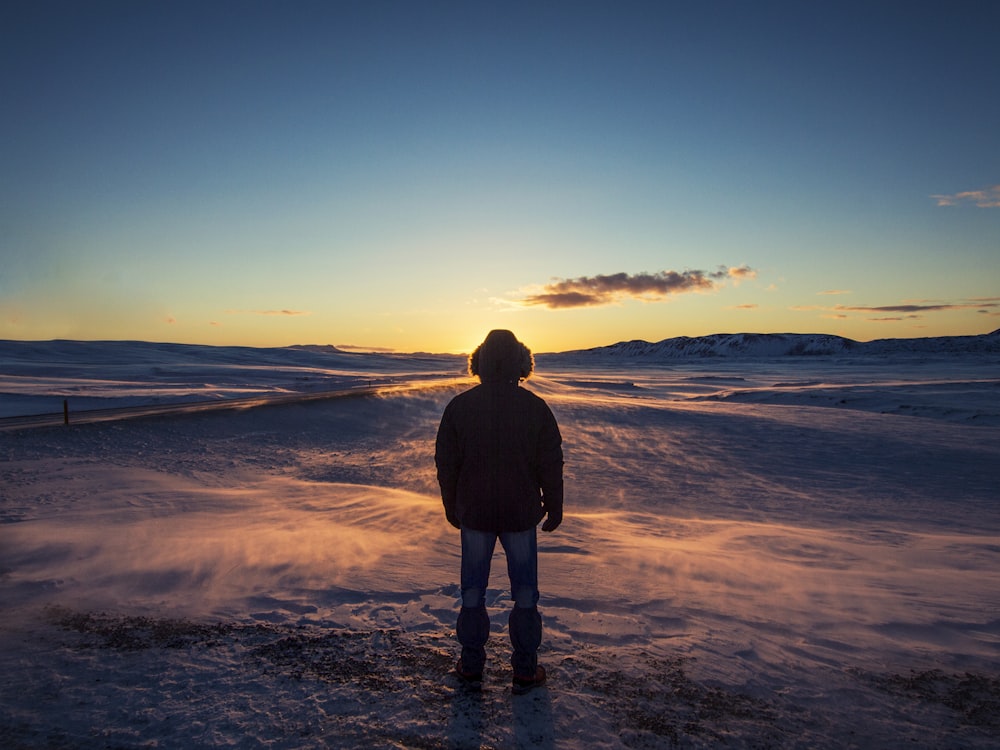 uomo in piedi su terreno coperto di neve durante l'alba