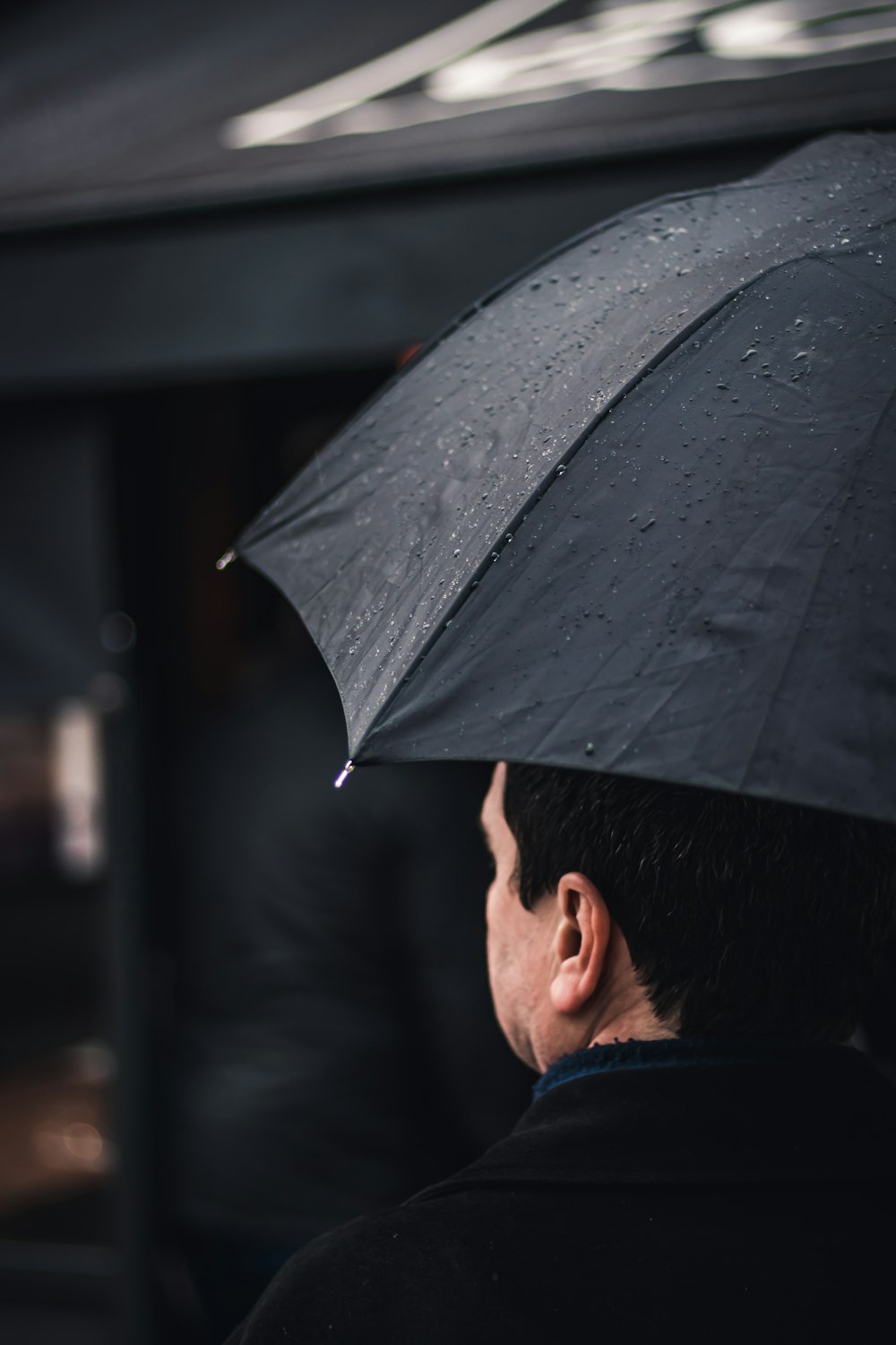 man wearing black top holding black umbrella walking near black awning