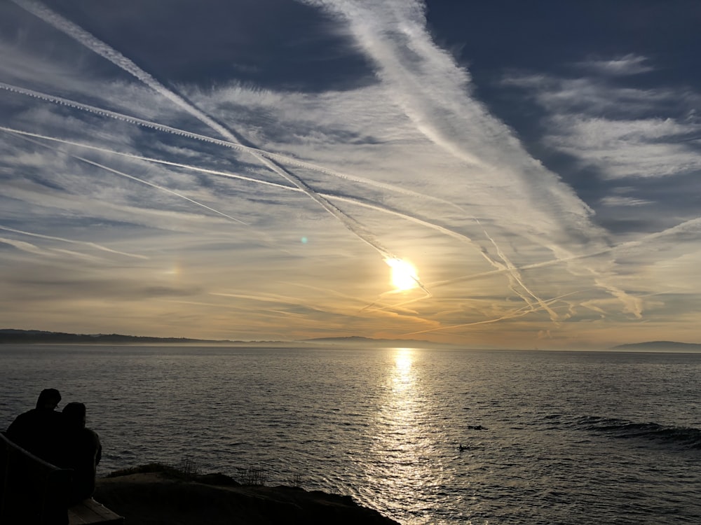 homme et femme regardant le coucher du soleil près du plan d’eau