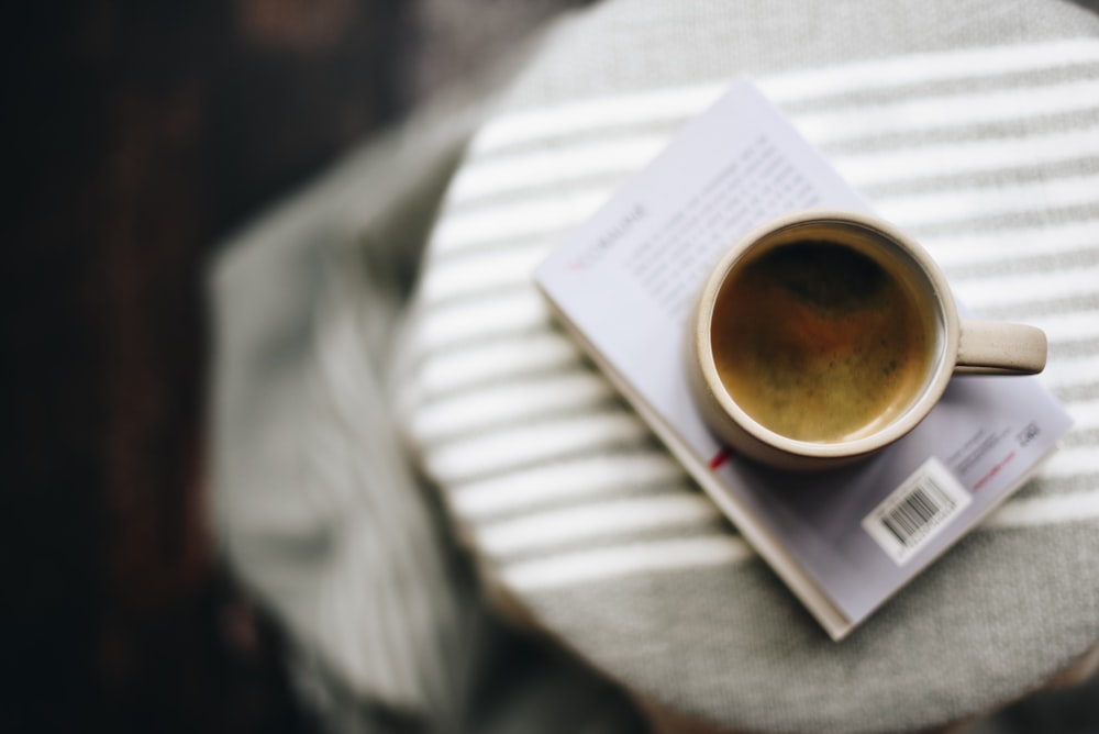 white ceramic mug with coffee on book