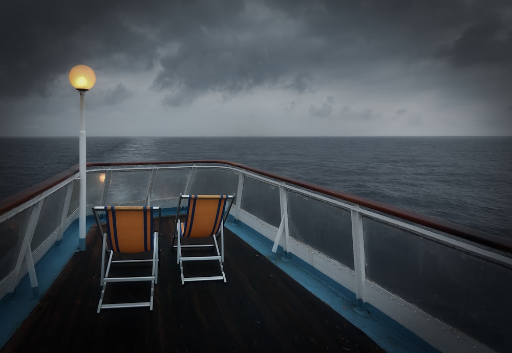 灰色の空の下、水域に囲まれたボートの上の茶色と白の折りたたみ椅子2脚