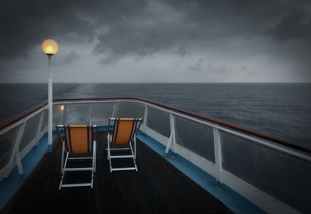 two brown and white folding chairs on boat surrounded by body of water under gray sky