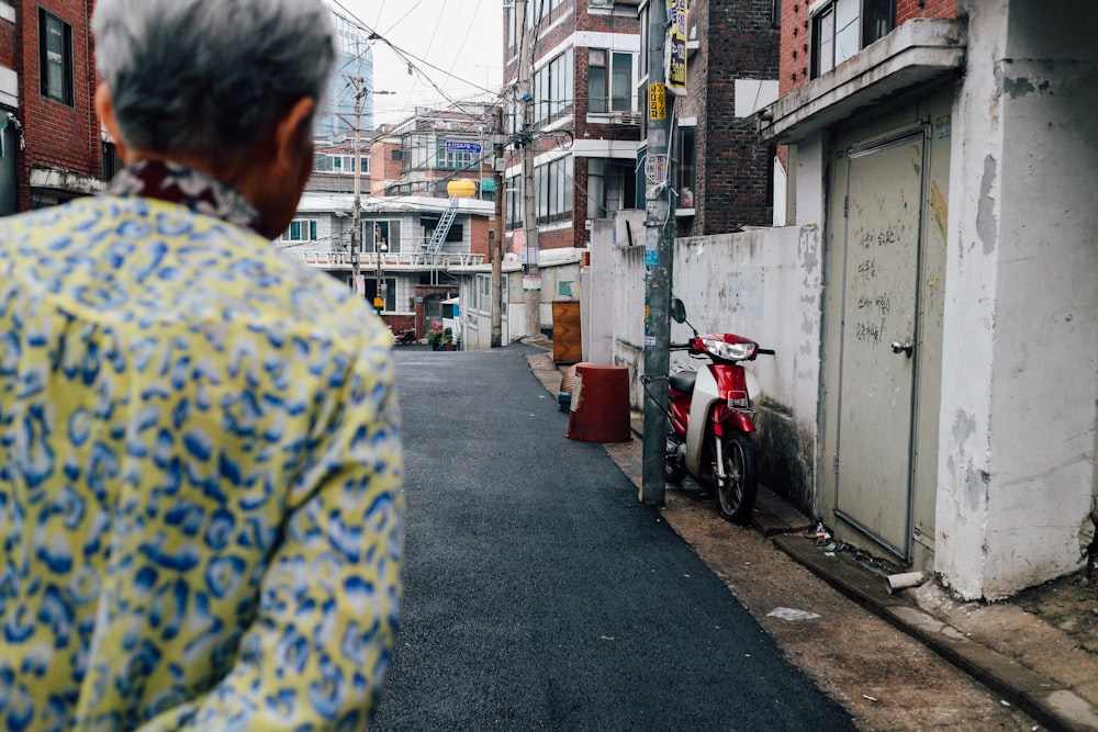 person walking on grey concrete road in front of red and white motorcycle during daytime