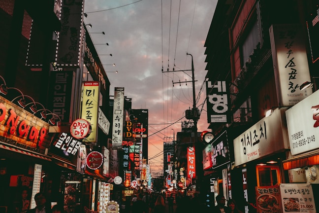 A glowing storefront sign with vibrant colors illuminating a busy street at dusk.