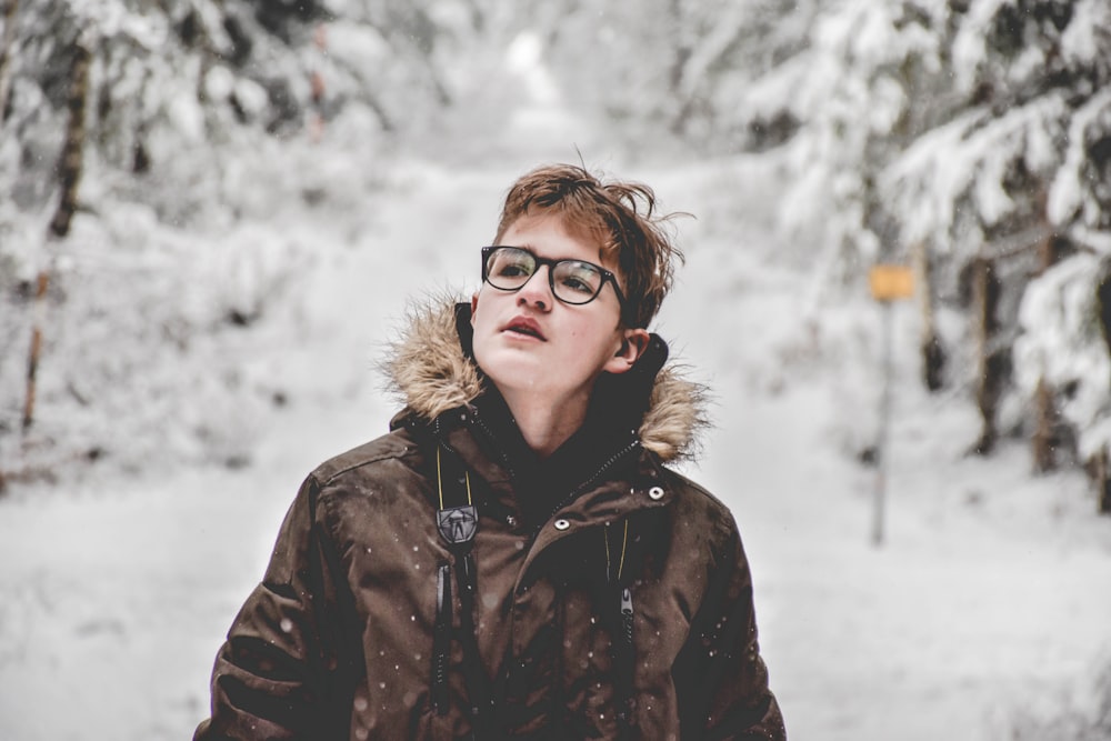 man wearing black hooded jacket standing near tall trees covered in snow during daytime