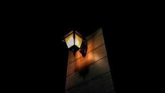 An outdoor wall lantern casting a gentle glow over a rustic porch at dusk.
