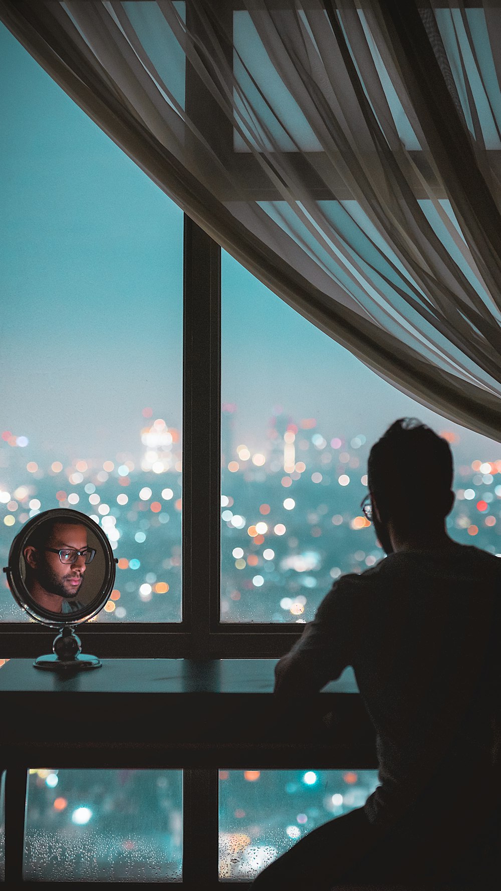 man sitting in front of black wooden table with face reflecting on round vanity table mirror