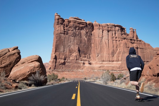 person in blue hoodie skateboarding near ruins in Arches National Park United States