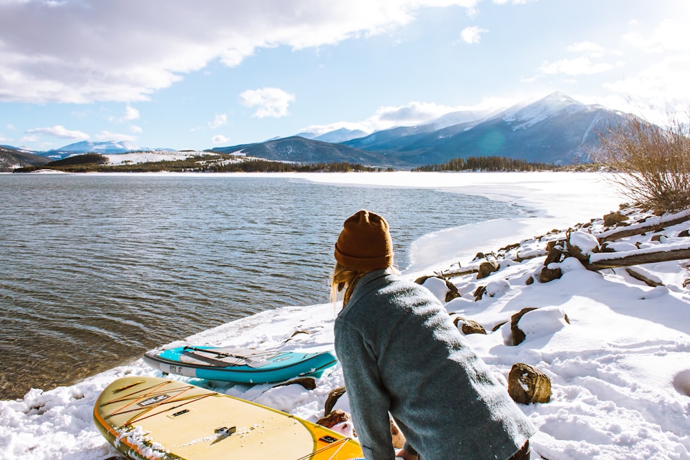 person standing beside yellow kayak and body of water near mountain under blue sky during daytime