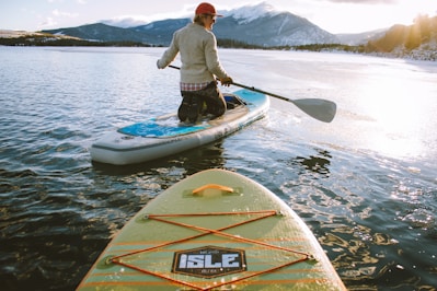 man wearing gray sweater kneeding on paddle board with holding oar during daytime