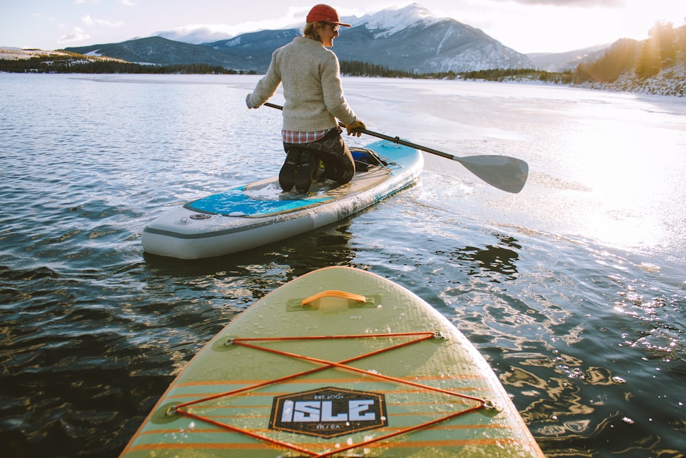 man wearing gray sweater kneeding on paddle board with holding oar during daytime
