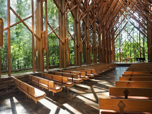A peaceful chapel interior with wooden pews and sunlight streaming through tall windows.