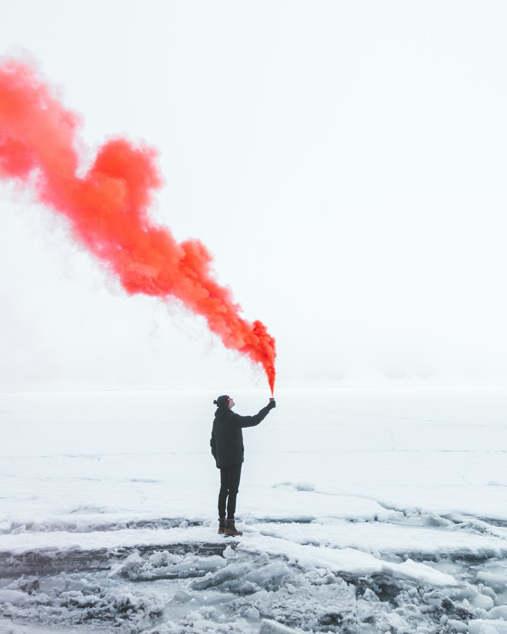 person wearing black jacket and holding red colored smoke flare during daytime