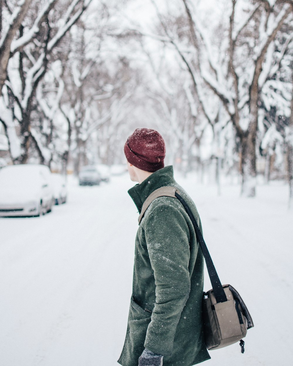 selective focus photography of man wearing coat and beanie standing watching vehicle on road