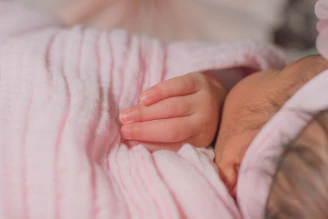 A softly lit photo of baby Saathvik smiling gently, wrapped in a cozy cream blanket.