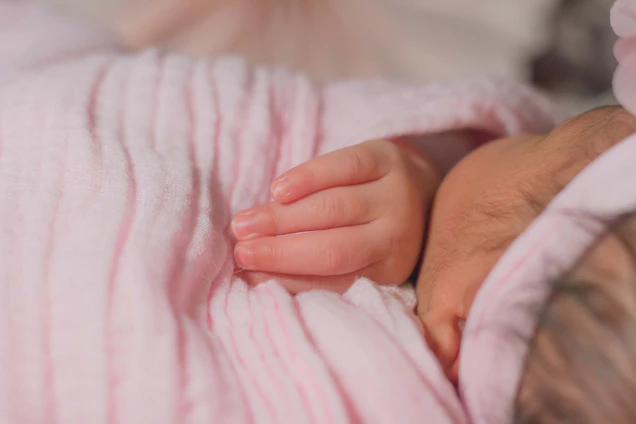 A softly lit photo of baby Saathvik smiling gently, wrapped in a cozy cream blanket.