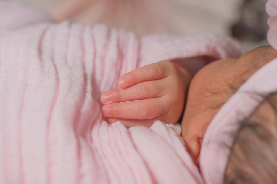 Soft pastel-toned photo of a newborn wrapped in a cozy blanket with a gentle smile