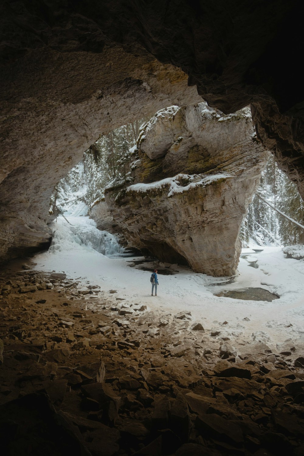 person standing between large rock formation filled with snow