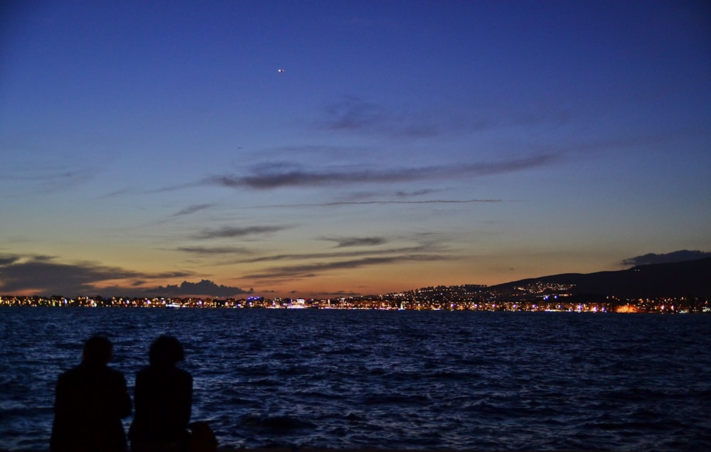 couple sitting near body of water watch city lights