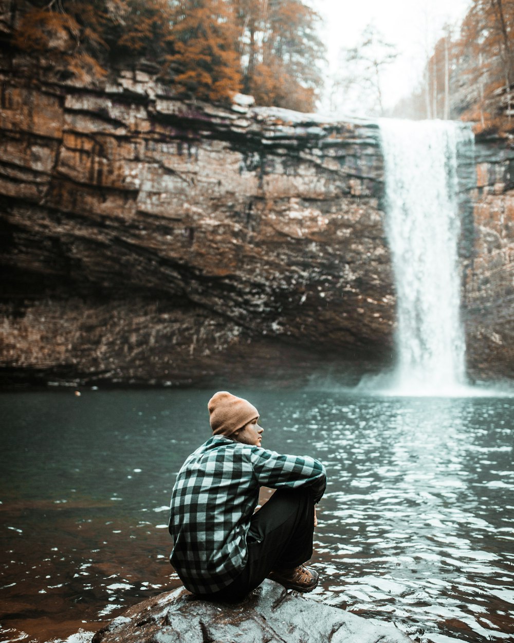 昼間、滝の近くの茶色の石の上に座っている男性