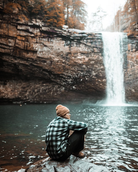 man sitting on brown stone near waterfall during daytime in Lookout Mountain United States