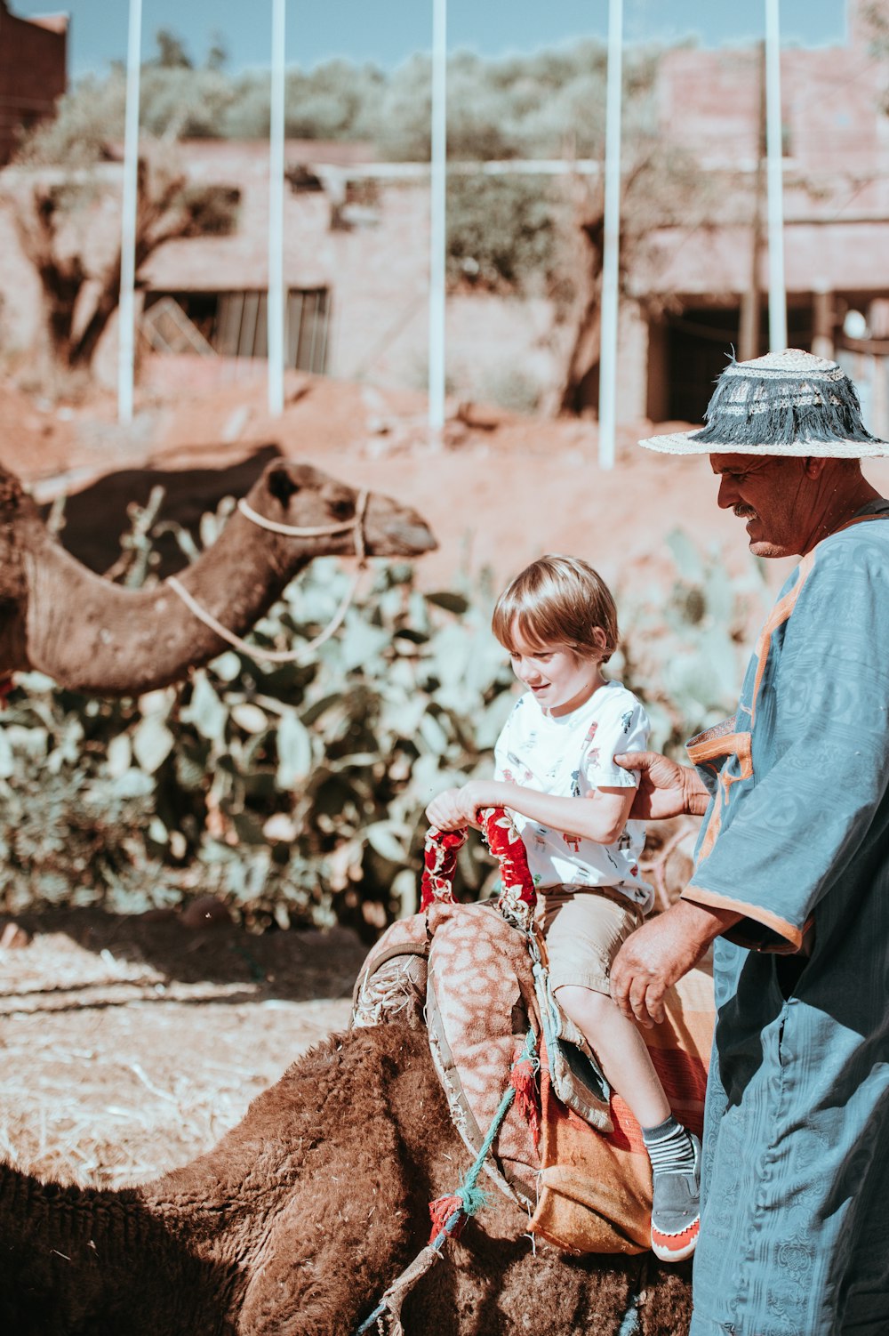 kid riding on brown camel beside man wearing green coat at daytime