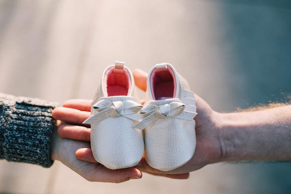 two person holding pair of baby's shoes