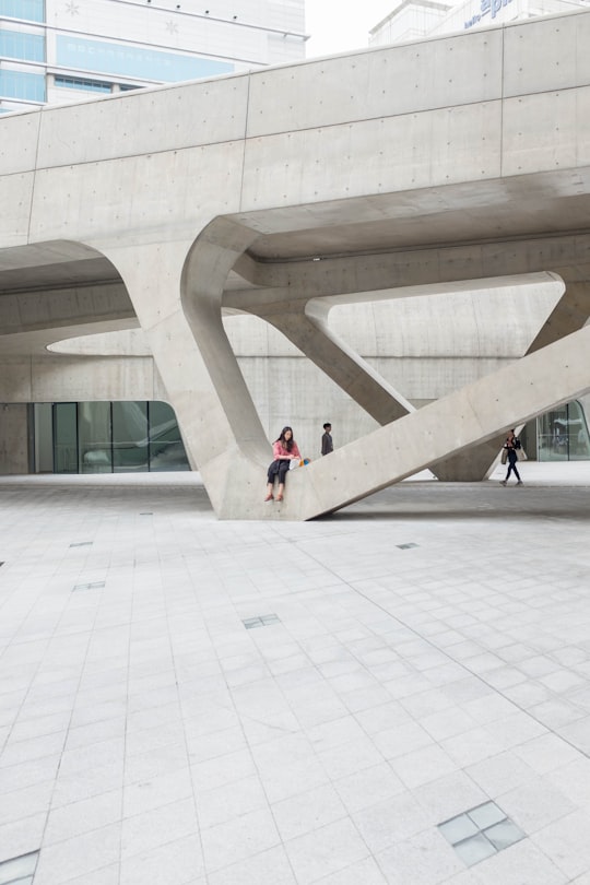 woman sitting on gray concrete formation during daytime in Dongdaemun Design Plaza South Korea