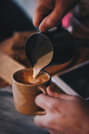 Barista carefully pouring latte art into a warm ceramic cup in a cozy café setting