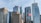 A skyline featuring modern skyscrapers with varied architectural designs, including logos of major corporations such as KPMG, BMO, and EY. A prominent Canadian flag is waving in the foreground. The sky is mostly clear, contributing to a well-lit scene.