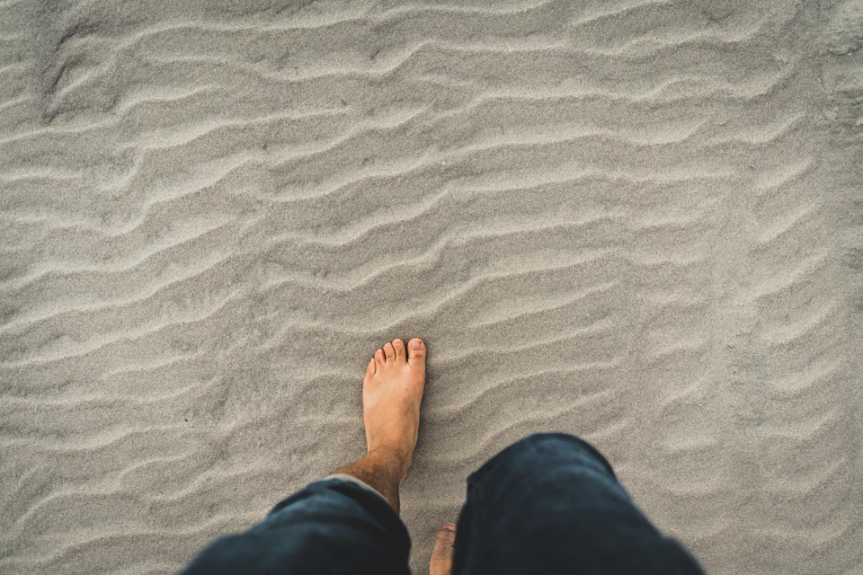 Person walking on sandy beach with toes visible and facing right side of frame