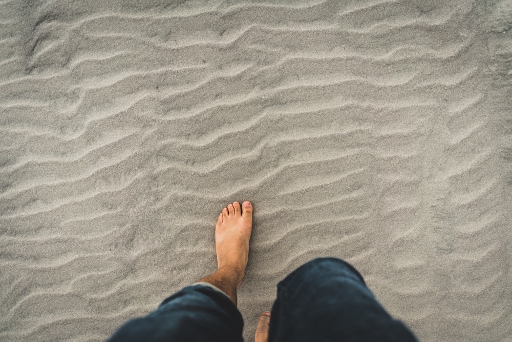 homme en jean bleu marchant dans le sable