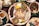 A variety of traditional dishes are arranged on a wooden table. The central platter contains slices of sausage, fried pork rinds, grilled meat, and various dipping sauces. Surrounding it are additional dishes with spices, vegetables, and garnishes, creating a colorful and appetizing display.