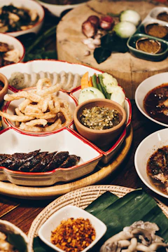 Close-up of hands serving a variety of traditional Thai and international dishes on a rustic wooden table.
