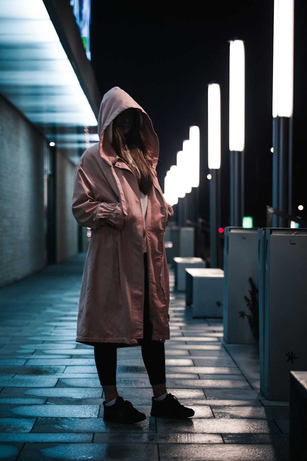 woman in pink hooded jacket standing on city sidewalk