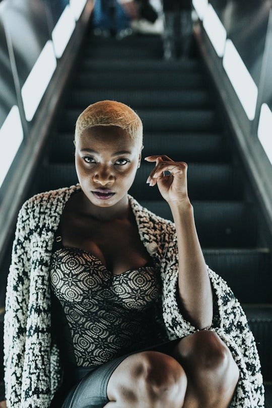 white haired woman wearing black and white sweetheart top and white and black cardigan sitting on black escalator in Downtown United States