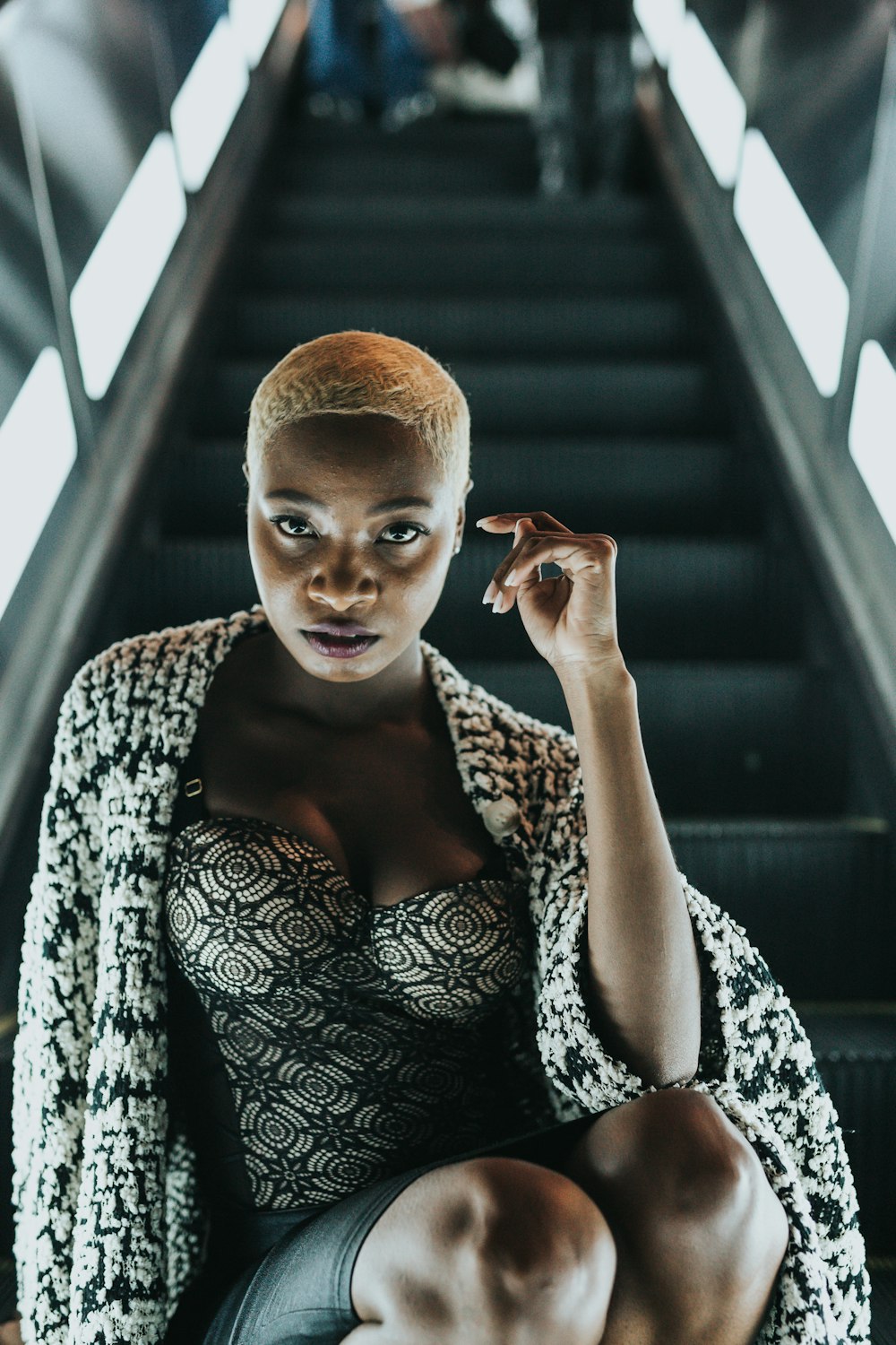 white haired woman wearing black and white sweetheart top and white and black cardigan sitting on black escalator