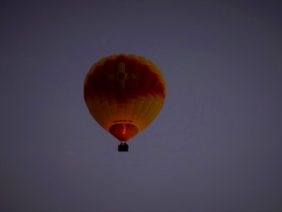A hot air balloon with yellow and red stripes floats against a dark, clear sky. The logo of a company is visible on the balloon's surface.