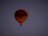 A hot air balloon with yellow and red stripes floats against a dark, clear sky. The logo of a company is visible on the balloon's surface.