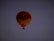 A hot air balloon with yellow and red stripes floats against a dark, clear sky. The logo of a company is visible on the balloon's surface.