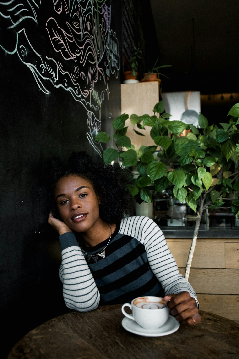 woman in white, black, and blue striped long-sleeved shirt sitting on chair in front of table holding white ceramic teacup