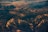 An aerial view of a rugged mountainous landscape with varying elevations and ridges. The sunlight casts a warm glow over the terrain, highlighting the textures and contours of the land.