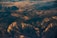 An aerial view of a rugged mountainous landscape with varying elevations and ridges. The sunlight casts a warm glow over the terrain, highlighting the textures and contours of the land.