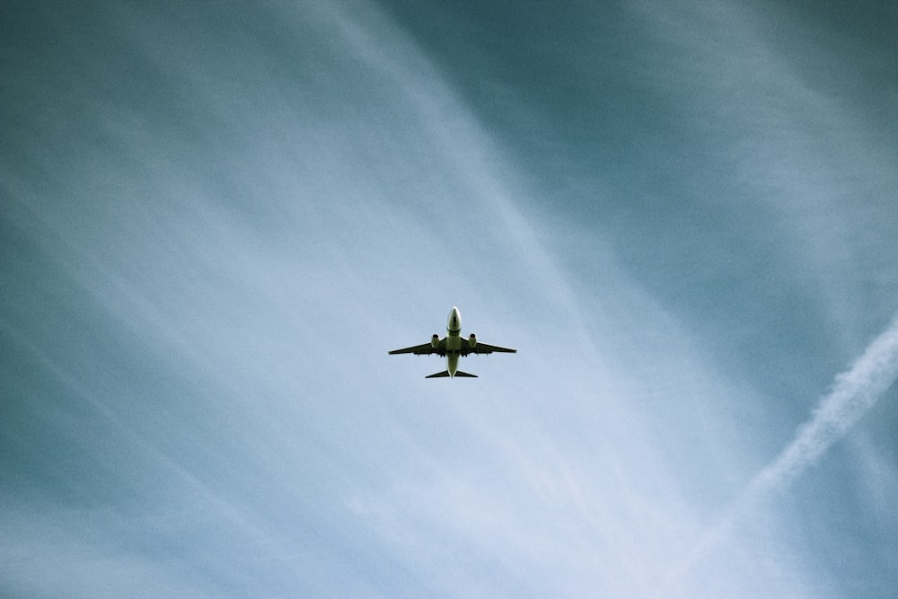 white airplane flying under blue sky