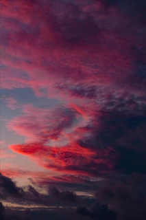A dramatic sky at twilight with glowing streaks of light weaving through dark clouds.