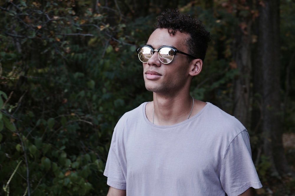 man in grey scoop-neck top standing in front of trees