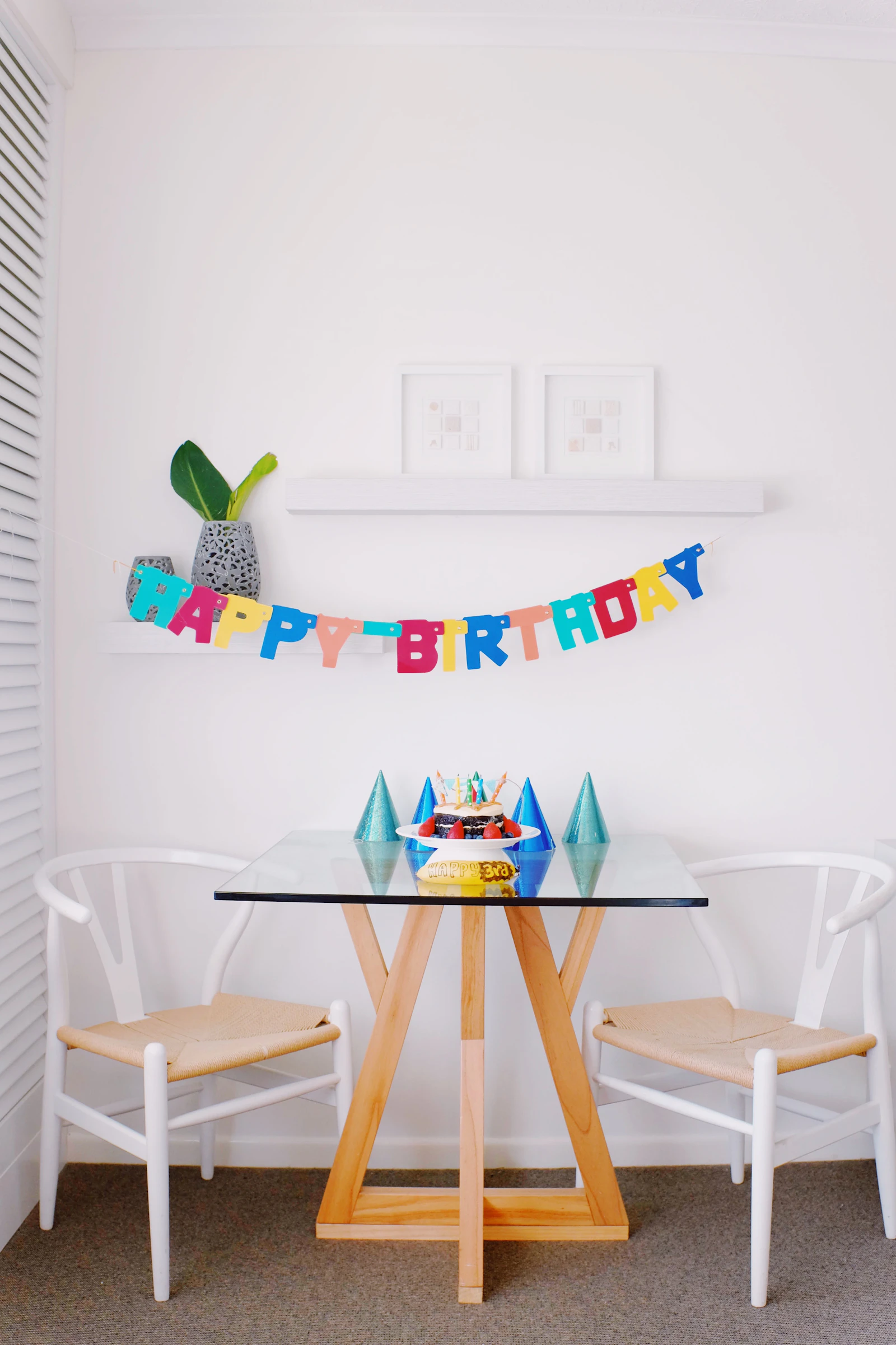 Rincón de cumpleaños con guirnalda de letras, gorritos y torta sobre la mesa